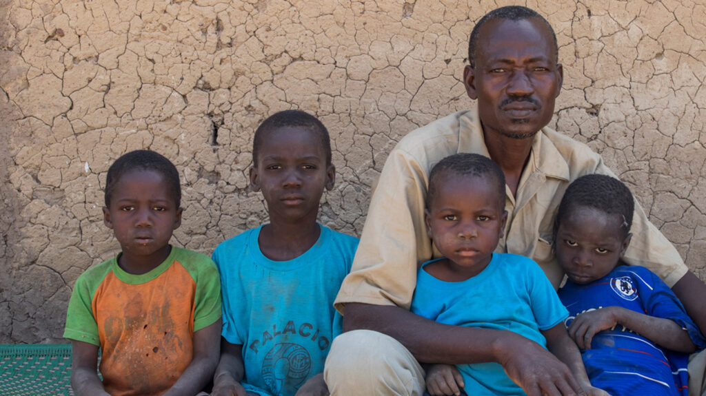 Soumalia sits with his four young grandchildren, two of which he is cuddling.
