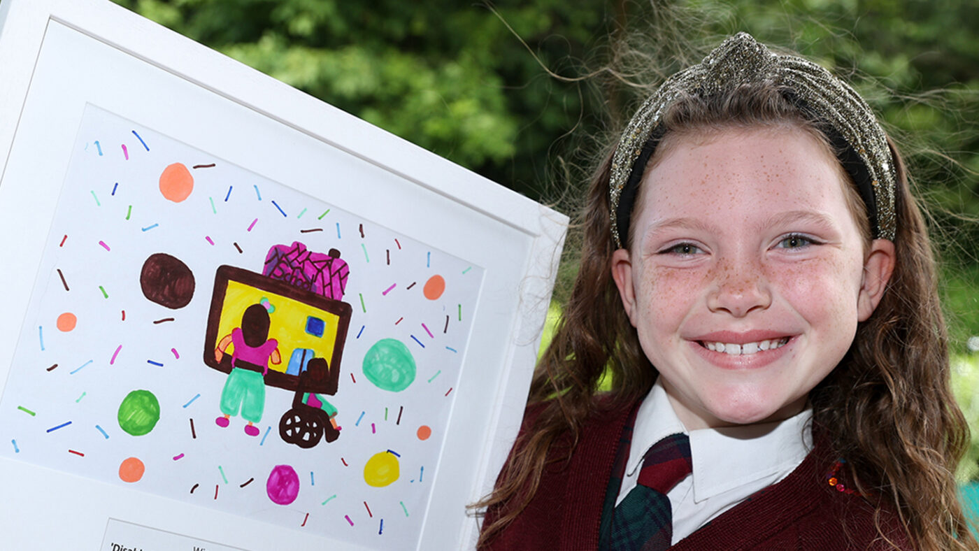 Eabha smiles while holding her colourful framed drawing.
