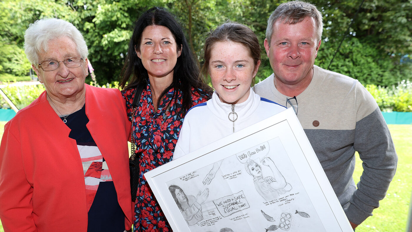 Sarah and three members of her family stand while she holds her framed pencil drawing.