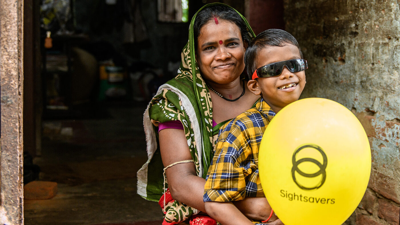 Sanjit smiles with his mother. He's wearing dark glasses. She's wearing a dark green headscarf.