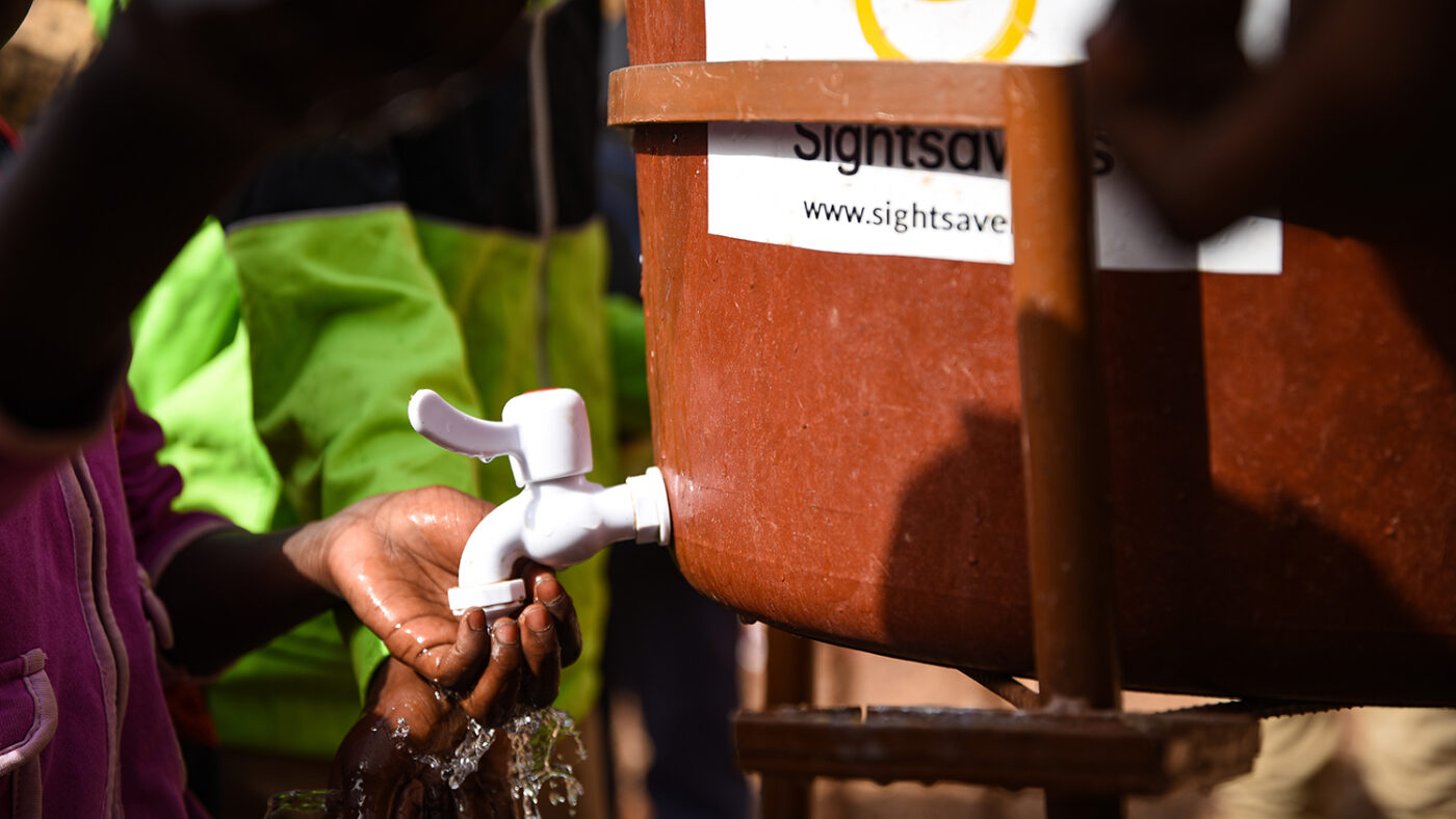Close-up of someone washing their hands under a Sightsavers-branded water tank.