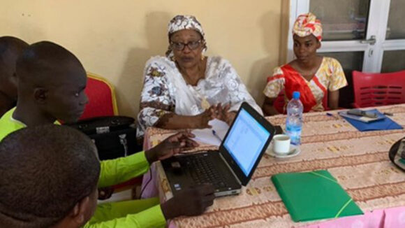 A group of people gather around a laptop at a VLR workshop.