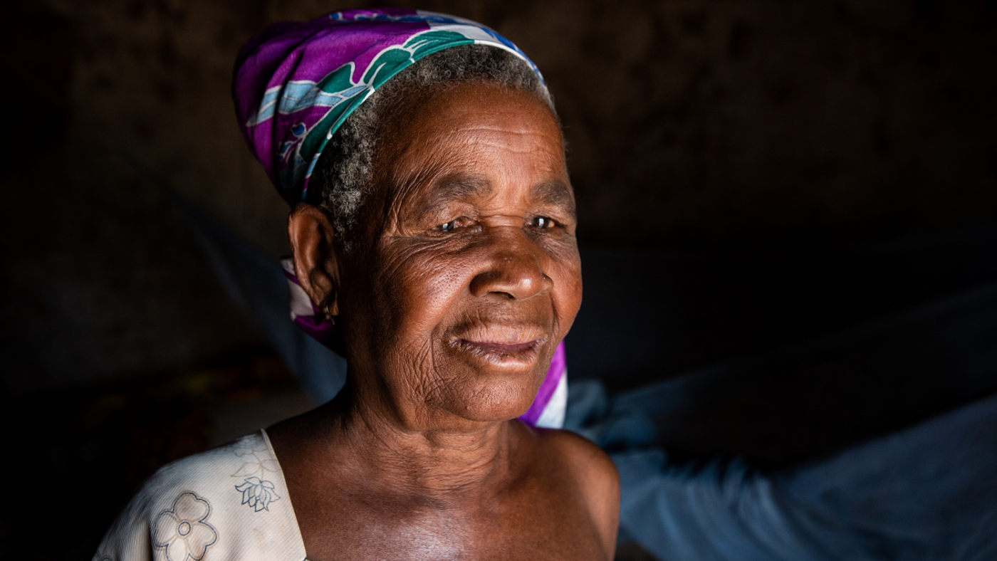 An older woman, Abena, faces outside in a dark room.
