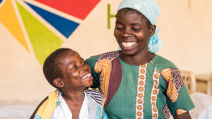 A young boy smiles up at his mother. They're both wearing colourful clothing.