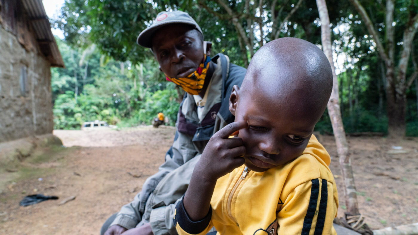 Mehnu sits outside with his father. He is itching his right eye