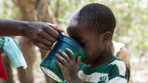 A young boy drinks water after receiving preventative medication for lymphatic filariasis in Guinea-Bissau.