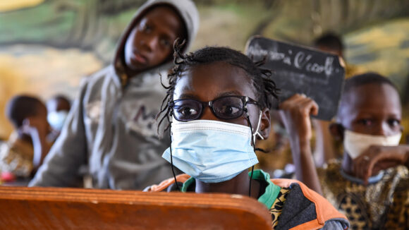 Maichata, who has a visual impairment, wears glasses and a surgical mask while sitting at her school desk.