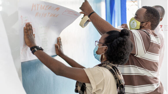 Two young people hold up flip charts on the wall as part of a training programme in Kenya.