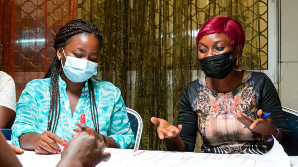 Leonie sits around a table during a meeting with a group of other women. She's talking animatedly.