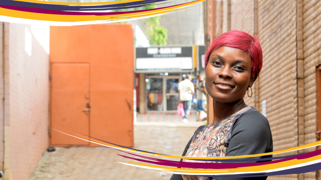 Leonie in Cameroon. She has vibrant red hair and is standing on city street.