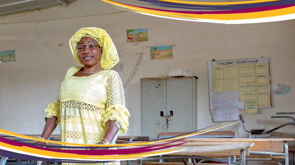 Isseu stands in a classroom holding her crutches. She's wearing a vibrant yellow dress and headscarf.