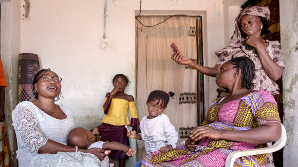 Isseu smiles with a group of women and children. She's holding a young baby.