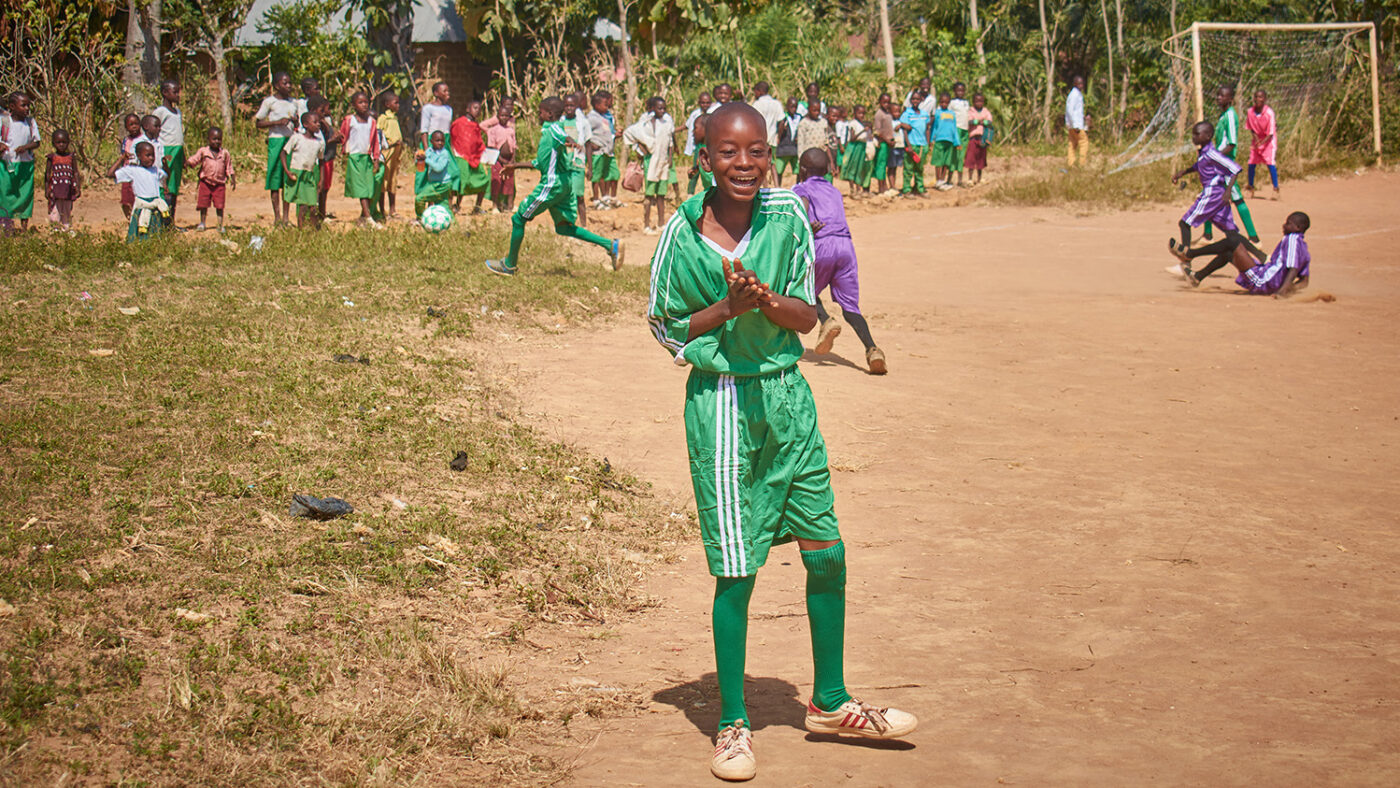 A boy wearing a sports kit poses and smiles.