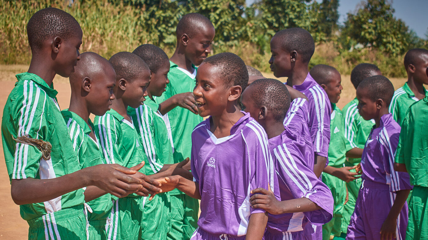 Schoolchildren wearing sports kits shake hands before playing a game of football.