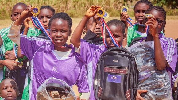 A group of girls and boys hold up medals after taking part in a football match.