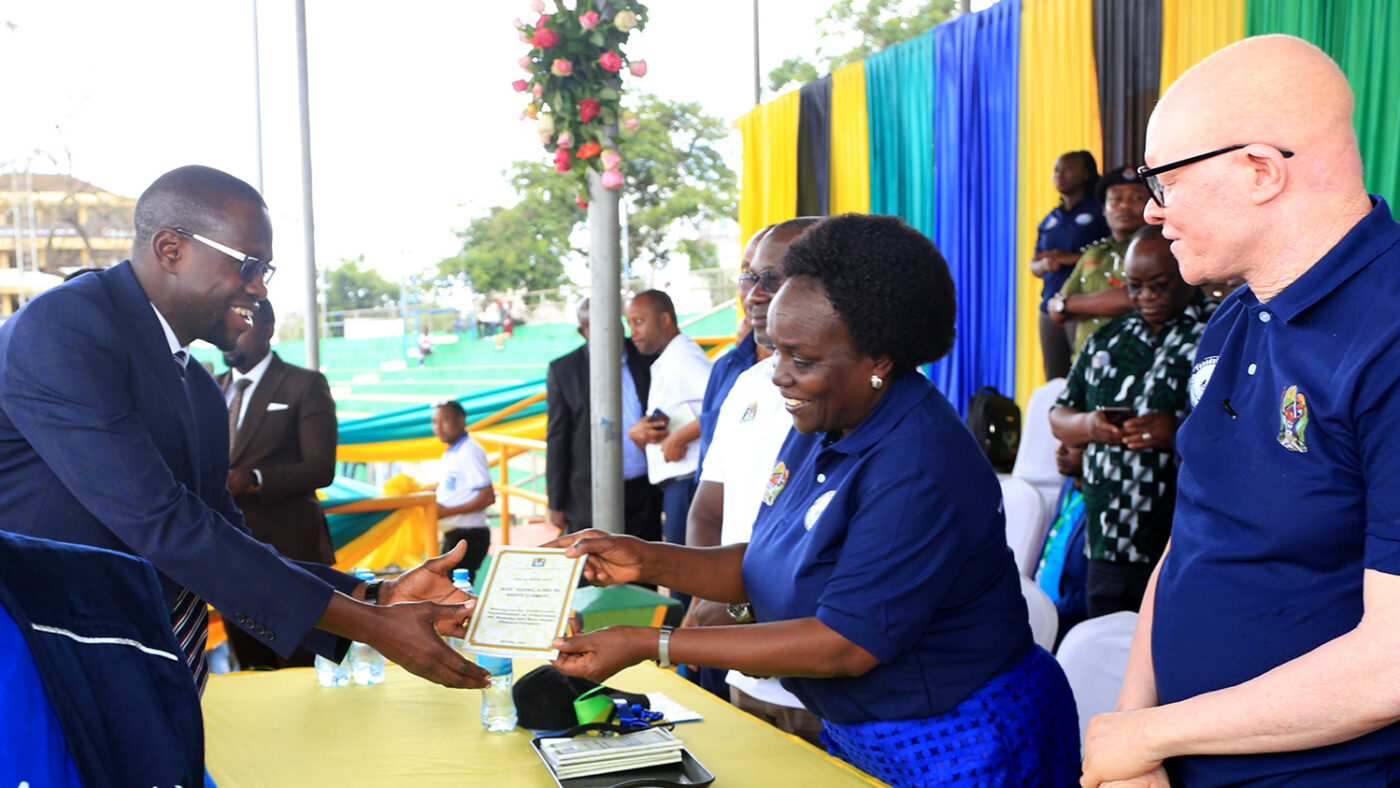 A woman presents a document to a man at an event about disability inclusion in Tanzania.