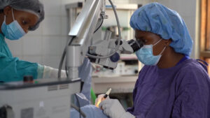 A still from the Sightsavers video, showing an eye surgeon in scrubs performing an eye operation.