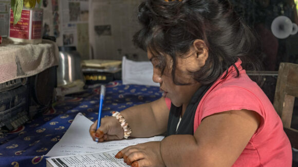 A woman of short stature signs paperwork at a table.