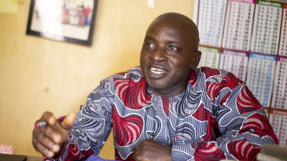 Head teacher Sabo talks animatedly. He's wearing a vibrant patterned shirt.