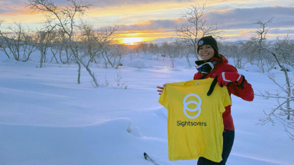 Sightsavers’ Ciara Smullen holds up a Sightsavers t-shirt while the sun rises behind her in the Arctic circle.