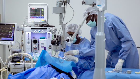 An eye surgeon operates on a patient. Another member of clinical staff assists them.