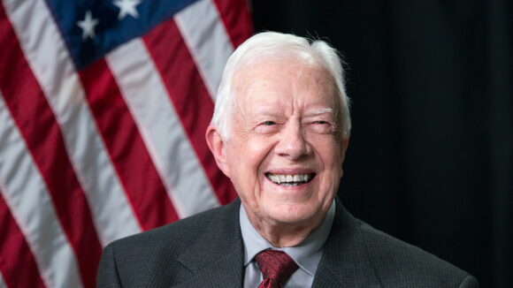 President Jimmy Carter smiles, with the US flag behind him.