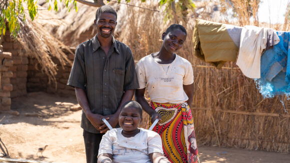 Enock, who uses a wheelchair, poses for a photo with two teachers from his inclusive school.