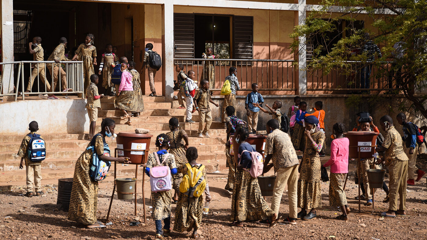 Schoolchildren wash their hands using water from outdoor taps.