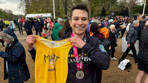 Matt celebrates after running the London Marathon by wearing a medal and holding up a Sightsavers top.