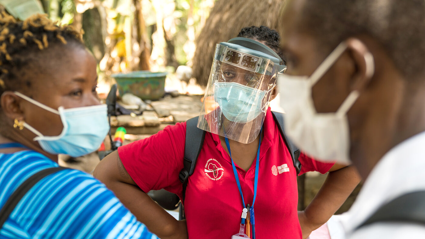 A group of researchers wearing face masks chat to each other outside in a village in Sierra Leone.
