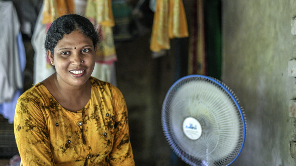 Community health worker Laboni sits next to a whirring fan.