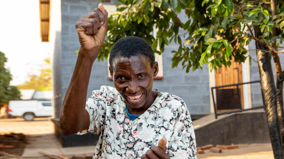 A woman in Malawi smiles and raises her arms in celebration.
