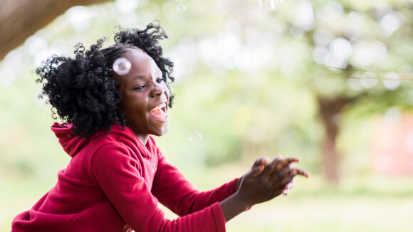 Young girl Luyando smiles while chasing bubbles outside her home.