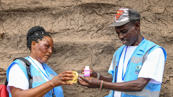 Two volunteers in Kenya wearing blue vests and holding medication.