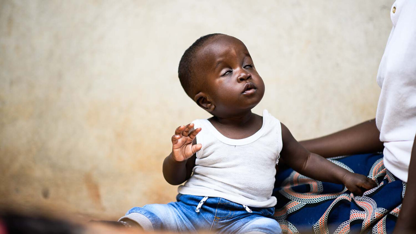 Chimwemwe looks up at his mother while sitting down.