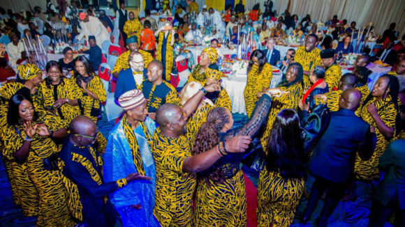A large party with lots of people dancing, wearing colourful yellow clothes.