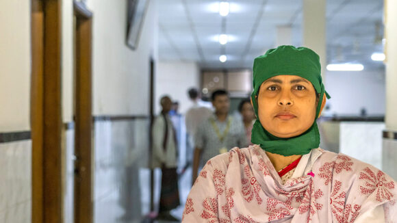 A female doctor stands in a hospital hallway wearing scrubs and protective gloves.