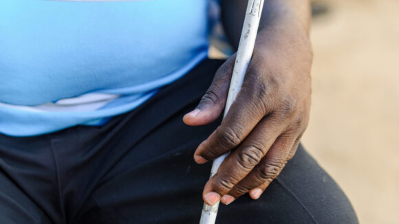 A close-up of a man's hand holding a white cane.