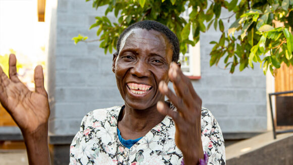 A woman in Malawi smiles at the camera and claps her hands.