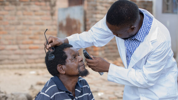 Ophthalmologist Alinafe uses a torch to check a man's eyes.