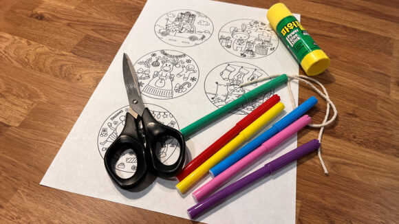 A collection of things needed to make the Christmas bauble: colouring sheet, pens, glue, string and scissors.