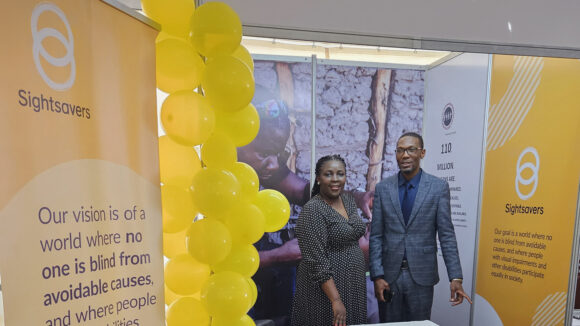 Hortance stands alongside a man at a Sightsavers event stand.