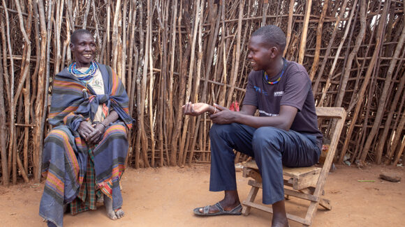 Maria and her son sit in chairs outside their home.