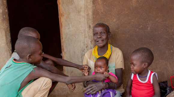 Veronica sits outside her home while holding a baby and surrounded by her grandchildren.