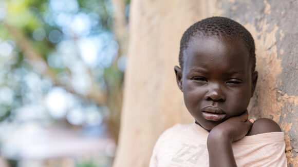 Six-year-old Happy outside her home in Uganda. She's squinting in the light.