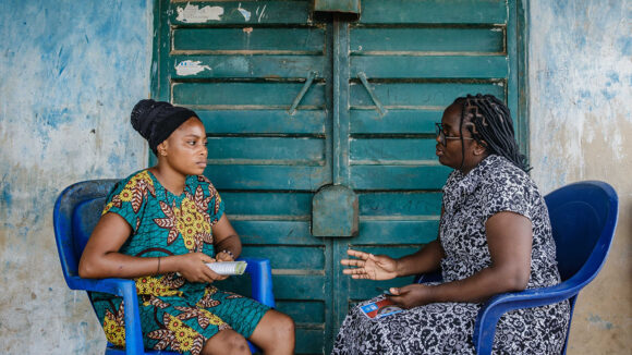 A female researcher speaks to a woman about her experience of female genital schistosomiasis.