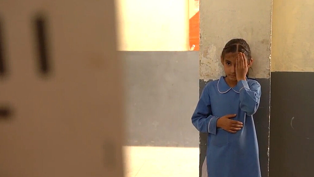 Nine-year-old Nayab stands with her left hand covering her eye, looking at an eye test chart.