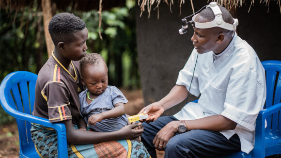 A mother holds her child as she speaks with Benjamin, a trachoma surgeon, during an eye screening in Uganda.
