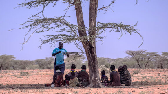 Community volunteer Richard Lowoto with a group of patients and their families seated under a shady tree in Turkana, Kenya.