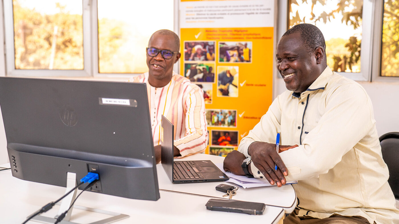 Didier and Emile sit behind a desk to analyse NTD data on a computer screen.
